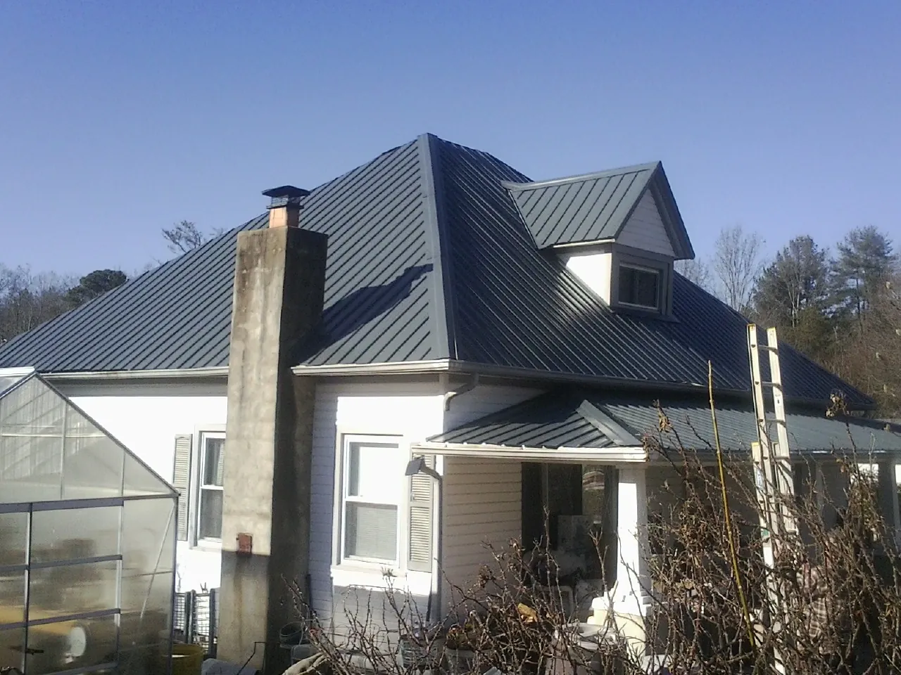 Dark blue standing seam metal roof on a white farmhouse with dormer — Slate & Tile Roof Repair by Roofing Brothers in Turpin