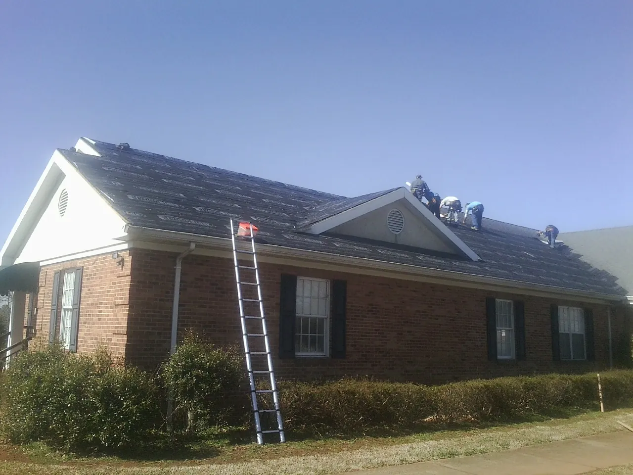 Crew tearing shingles off a brick ranch roof with a ladder set — Emergency Roof Repair work by our crew in Turpin