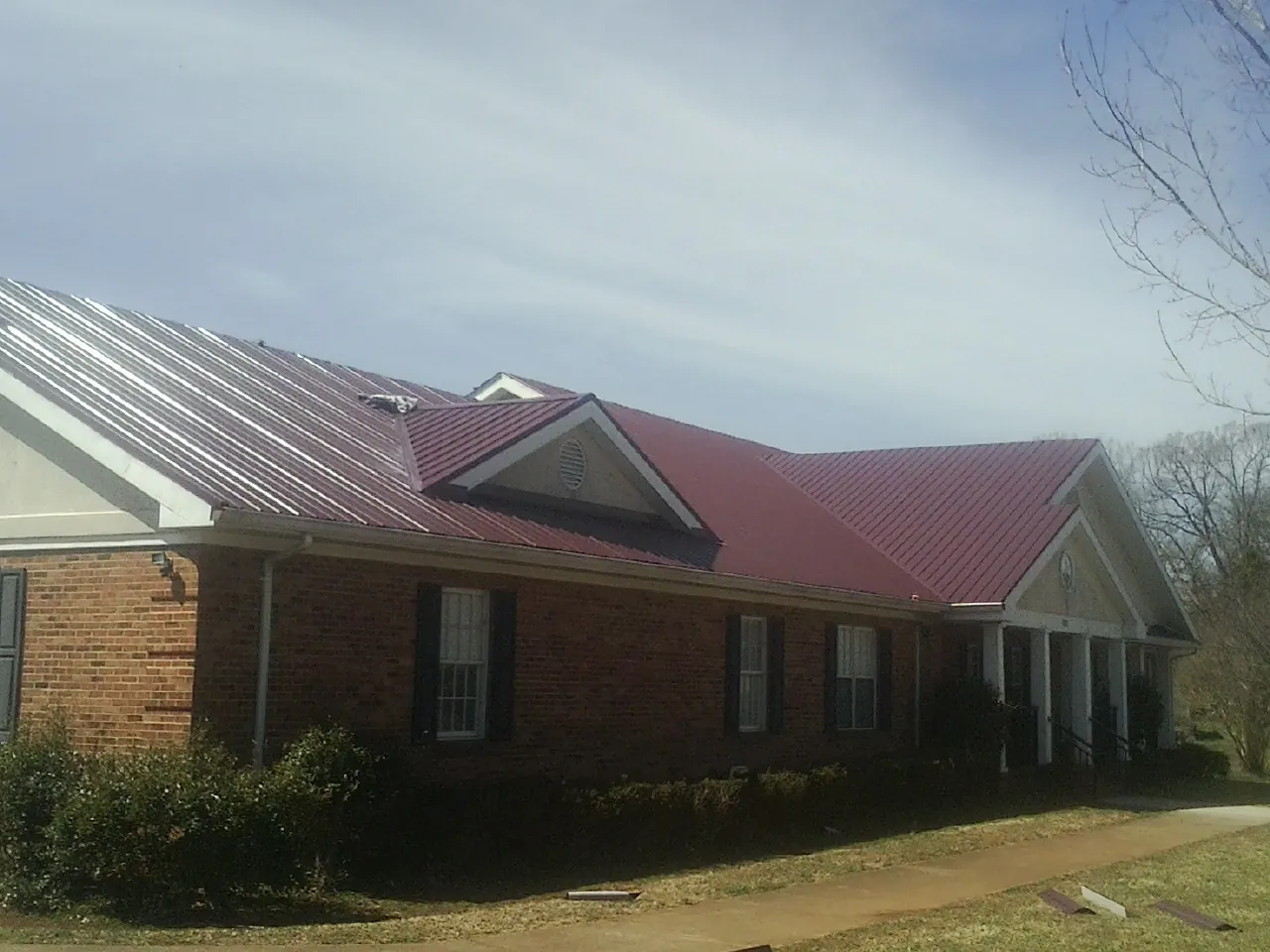 Red metal roof with gabled entries on a long brick building, from a Hail Damage Roof Repair job in Turpin