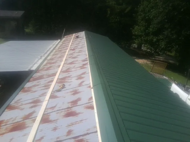 Old rusted panels beside newly installed green metal roofing — Wind Damage Roof Repair by Roofing Brothers in Turpin