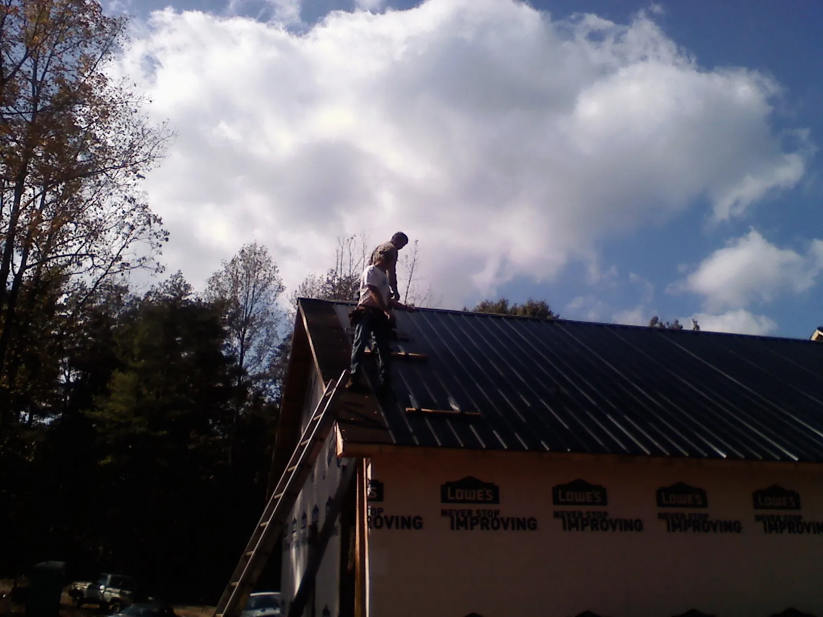 Roofer fastening dark metal panels high against a cloudy sky, from a Roof Inspection job in Turpin