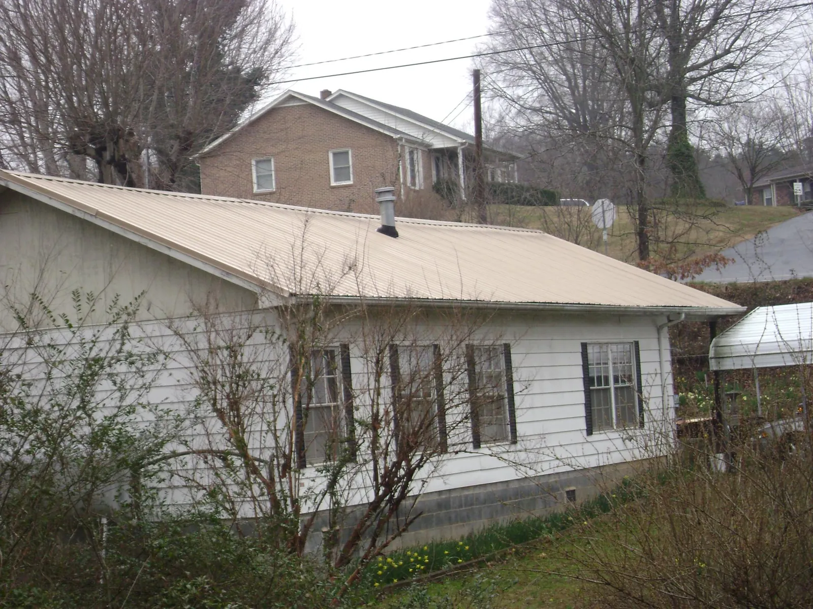 Tan metal roof on a white sided house set into a hillside — Commercial Roofing by Roofing Brothers in Turpin