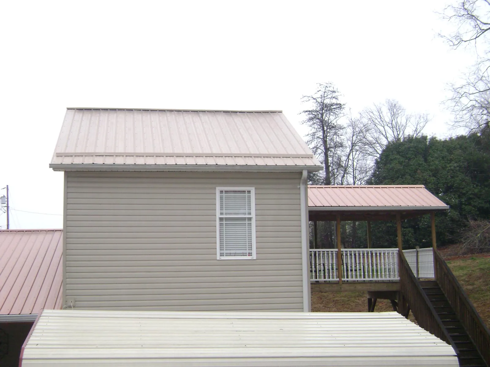 Tan metal roofs on a two story addition and attached porch, from a Roof Replacement job in Turpin